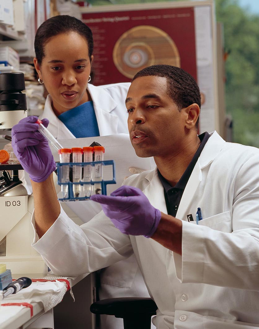 A male researcher checking test tubes while a female researcher looks on.